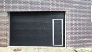 Newly installed black commercial garage door with a pass door, exterior view.