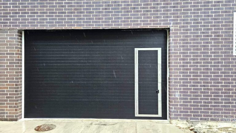 Newly installed black commercial garage door with a pass door, exterior view.